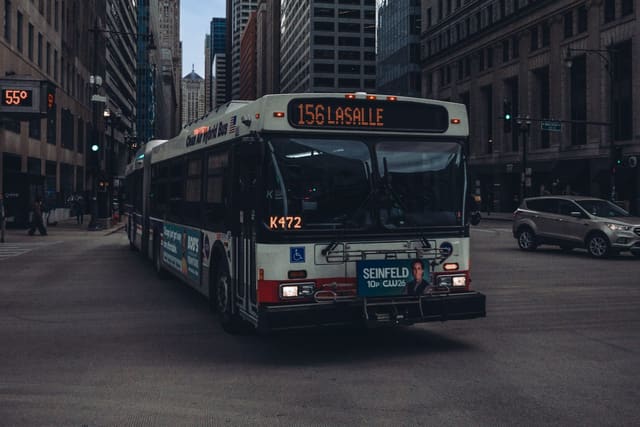 An articulated Chicago Transit Authority bus showing route 156 LaSalle crosses an intersection among downtown Chicago office towers.