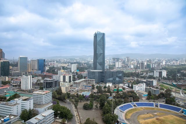 Aerial view of central Addis Ababa under cloud, with the glass tower of the Commercial Bank of Ethiopia headquarters at the centre and Addis Ababa Stadium in the foreground