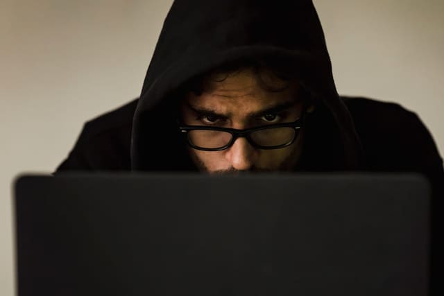 A person in a dark hood working on a laptop