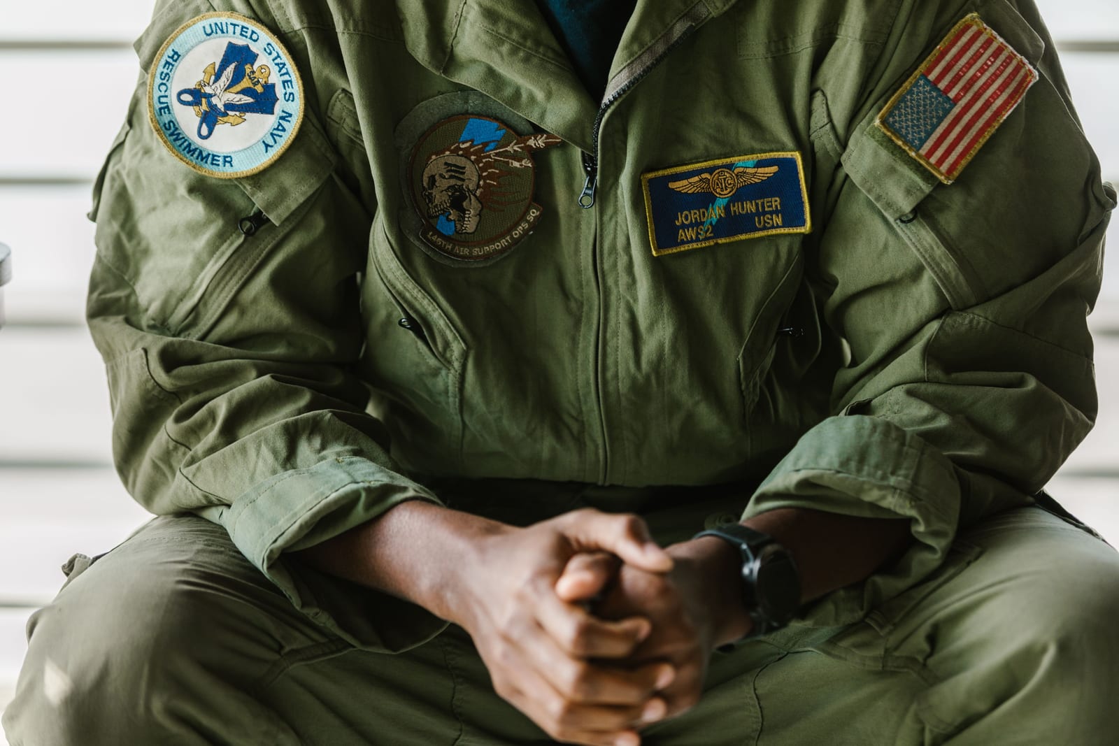A service member in a flight suit with unit patches, hands clasped